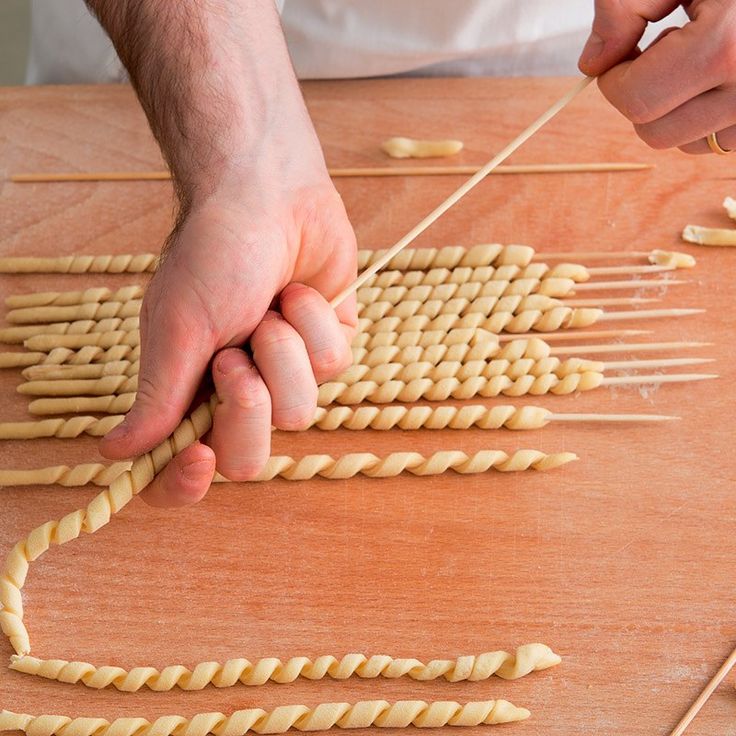 a person is making pasta on a wooden table with two hands and sticks sticking them in the shape of an arrow