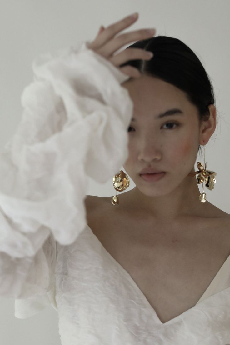 a woman in a white dress holding her hands up to her face