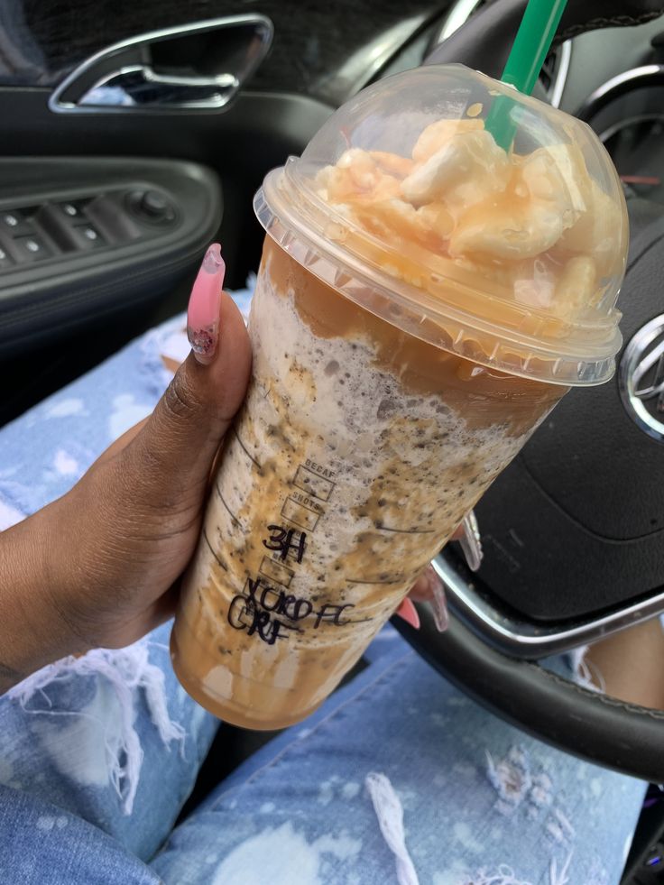 a woman holding up a drink in her hand while sitting in the backseat of a car