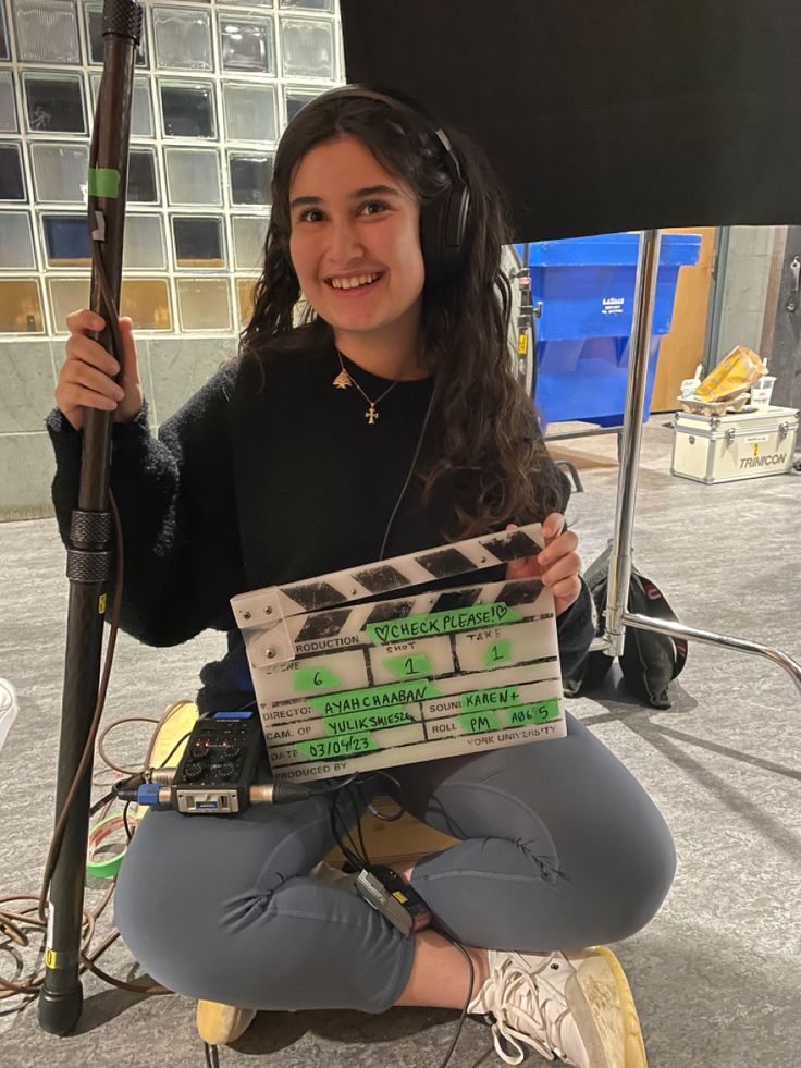 a woman sitting on the ground holding a clapper and headphones in her hands