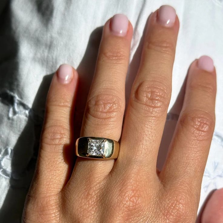 a close up of a person's hand wearing a gold ring with a diamond