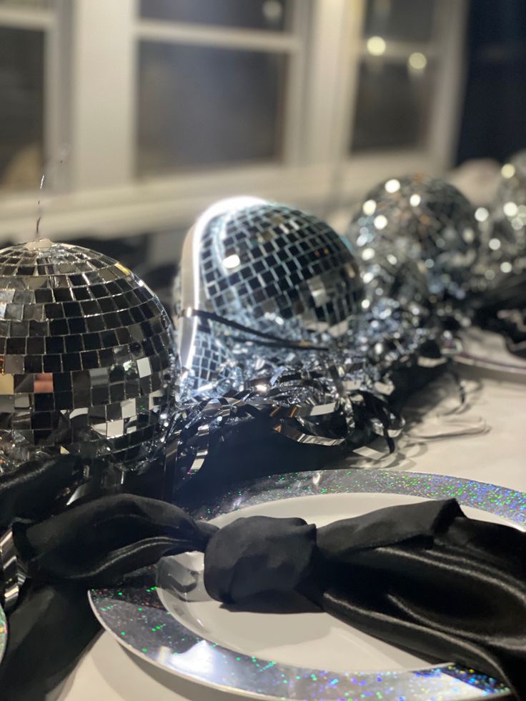 disco ball decorations on a table with black ribbon and silver plates in the foreground