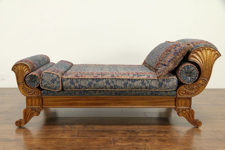 an ornate wooden chaise lounge with blue and red pillows on it's back