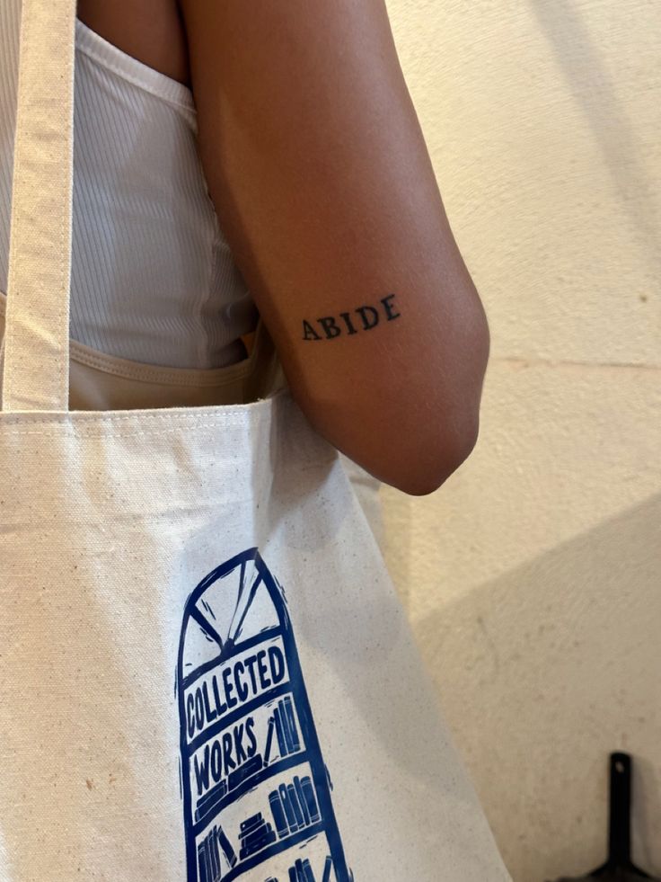 a woman with a tattoo on her arm holding a tote bag that reads, collected works