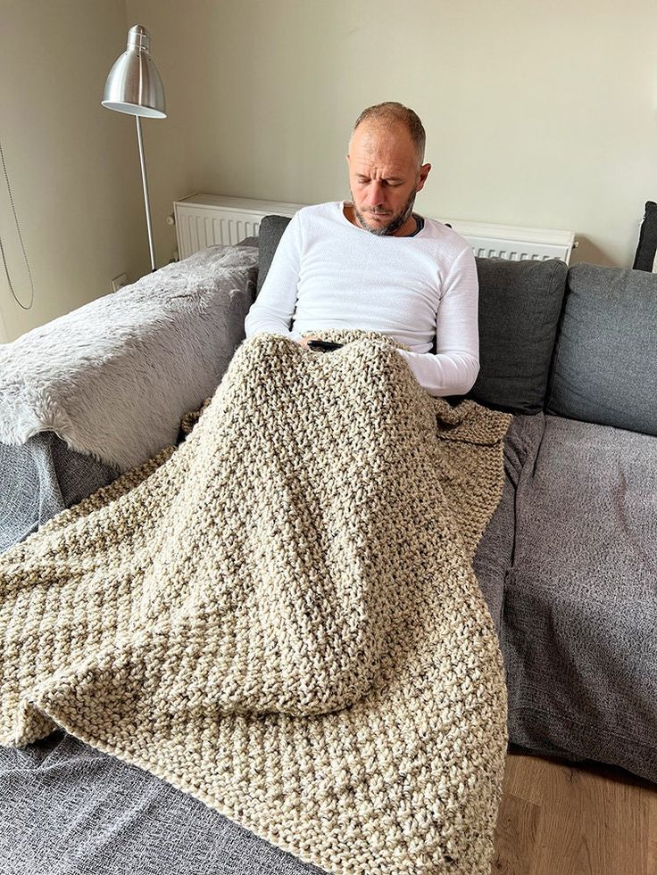 a man sitting on a couch covered in a crocheted blanket