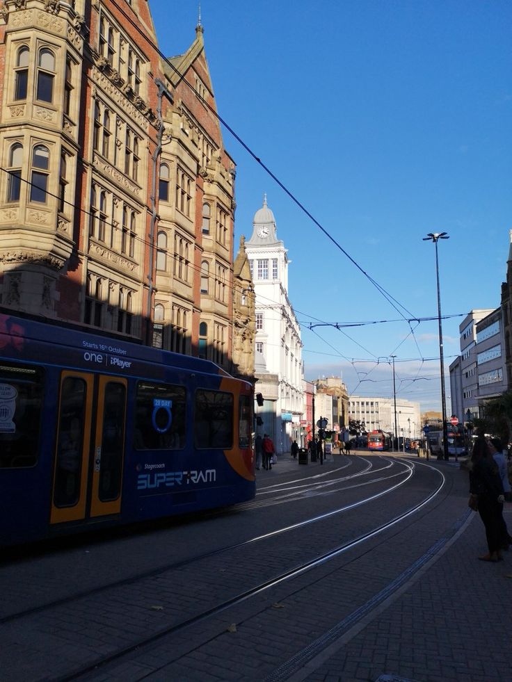 a blue and yellow train traveling down a street next to tall buildings on a sunny day