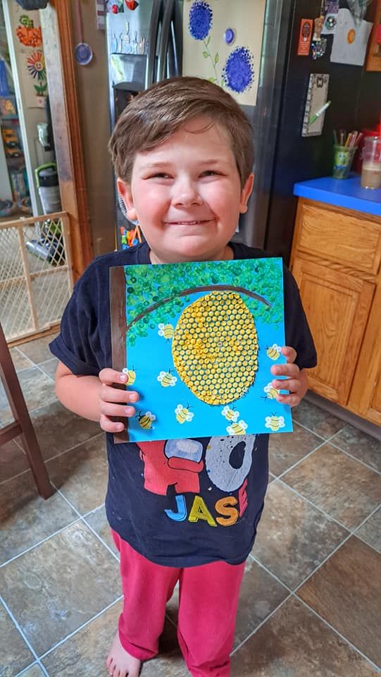 a young boy holding up a painting in the kitchen