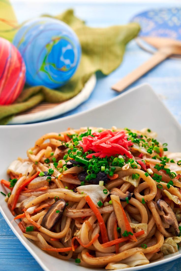 a white plate filled with noodles and vegetables on top of a blue table cloth next to other plates