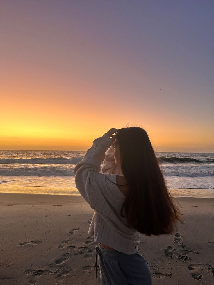 a woman standing on top of a sandy beach next to the ocean at sun set