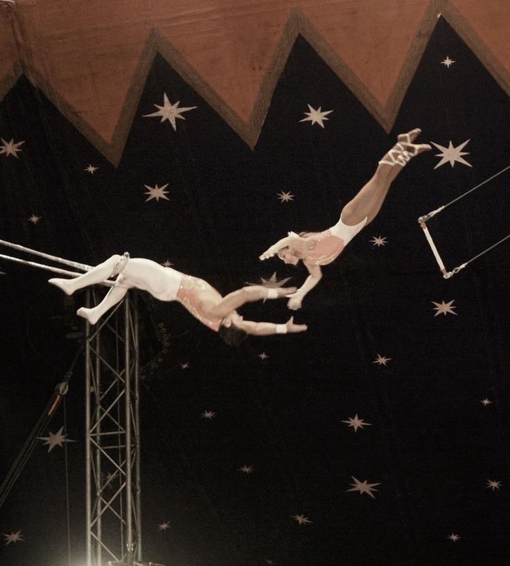 two men performing aerial acrobatic tricks in front of an audience at a circus