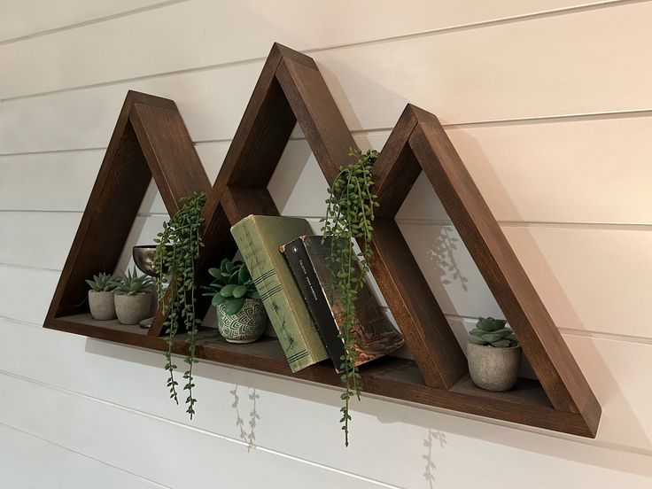 three wooden shelves with plants and books on them, hanging from the side of a wall