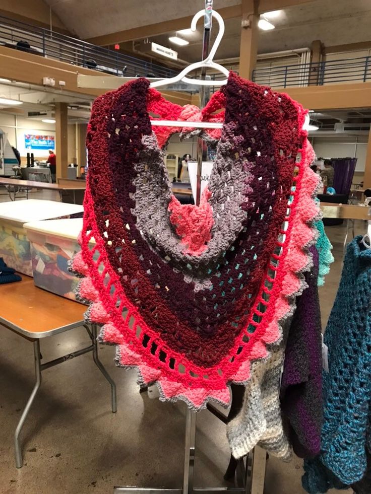 a crocheted shawl hanging from a rack in a room filled with tables and chairs