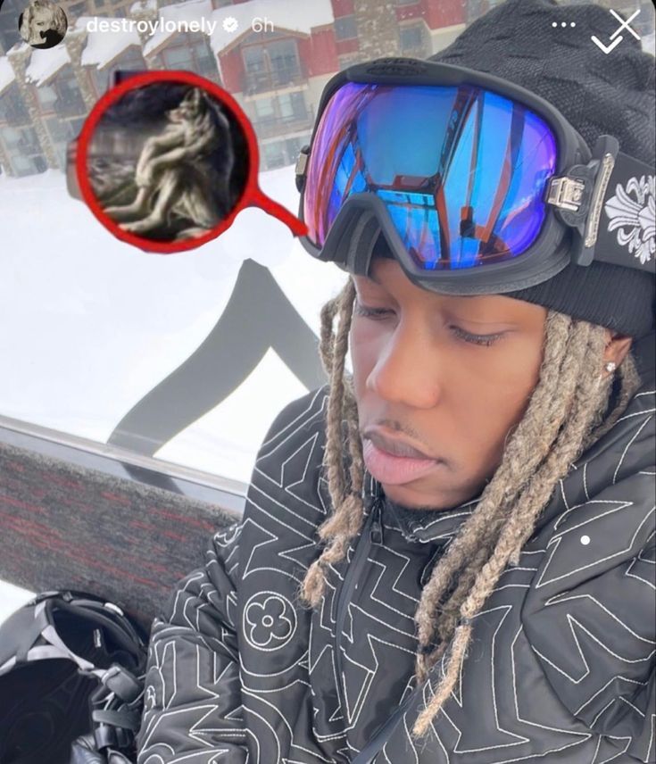 a young man with dreadlocks and ski goggles looking at his cell phone