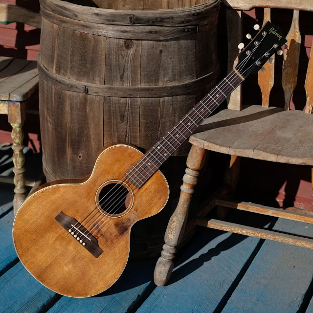 an acoustic guitar sitting on top of a wooden floor next to a barrel and chair