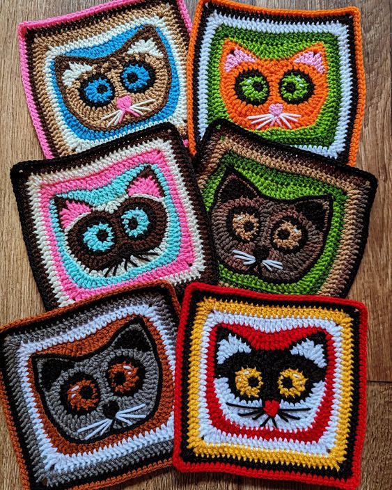 four crocheted coasters with cats on them sitting on a wooden table top