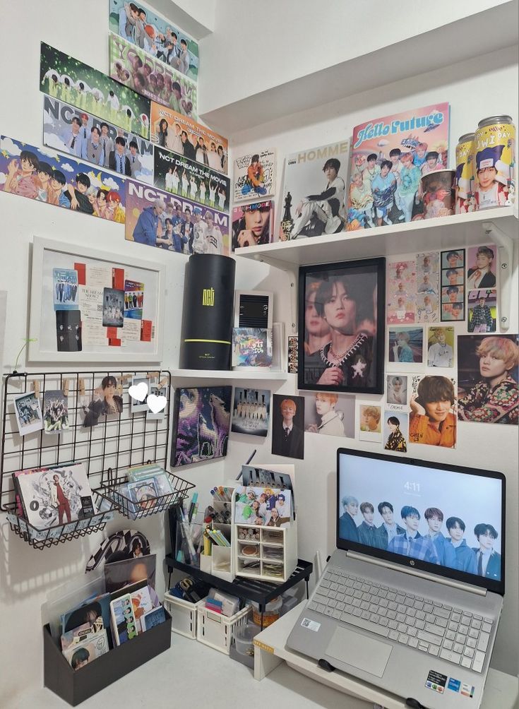 a laptop computer sitting on top of a desk next to a wall covered in pictures