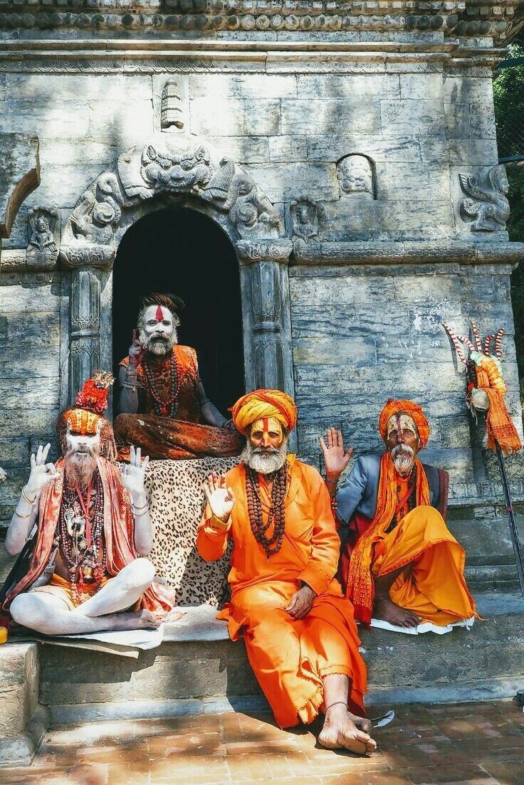 three men dressed in orange sit on steps with one holding his hand up to the sky