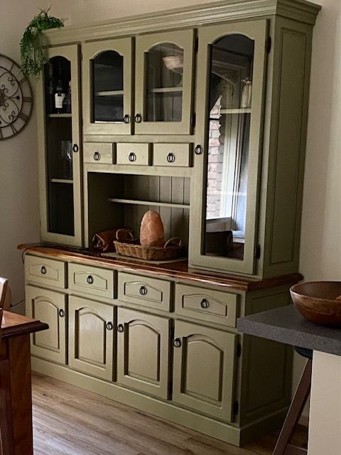 a green china cabinet with glass doors in a room next to a table and chair