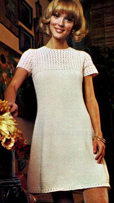 a woman standing next to a vase with flowers in it and wearing a white dress