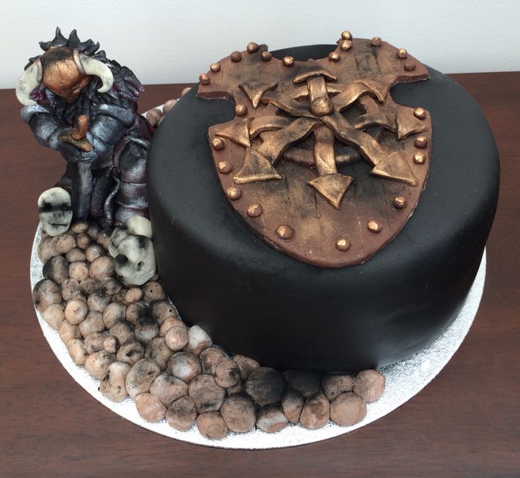 there is a black cake with gold decorations on the top, and a small figurine next to it