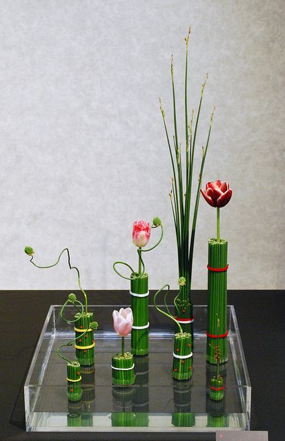 there are many vases with flowers in them on the glass table and one is green