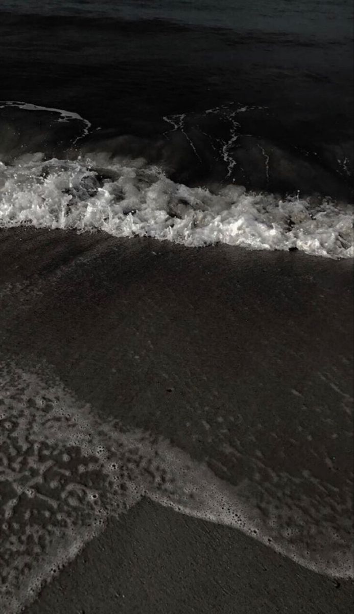 black and white photograph of waves coming in to the shore on a beach at night