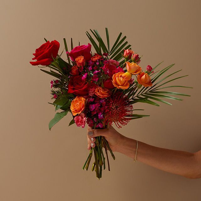 a person holding a bouquet of flowers in their hand with the background beige wall behind them