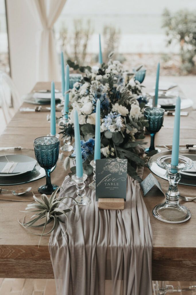 the table is set with blue candles, flowers and napkins for an elegant dinner