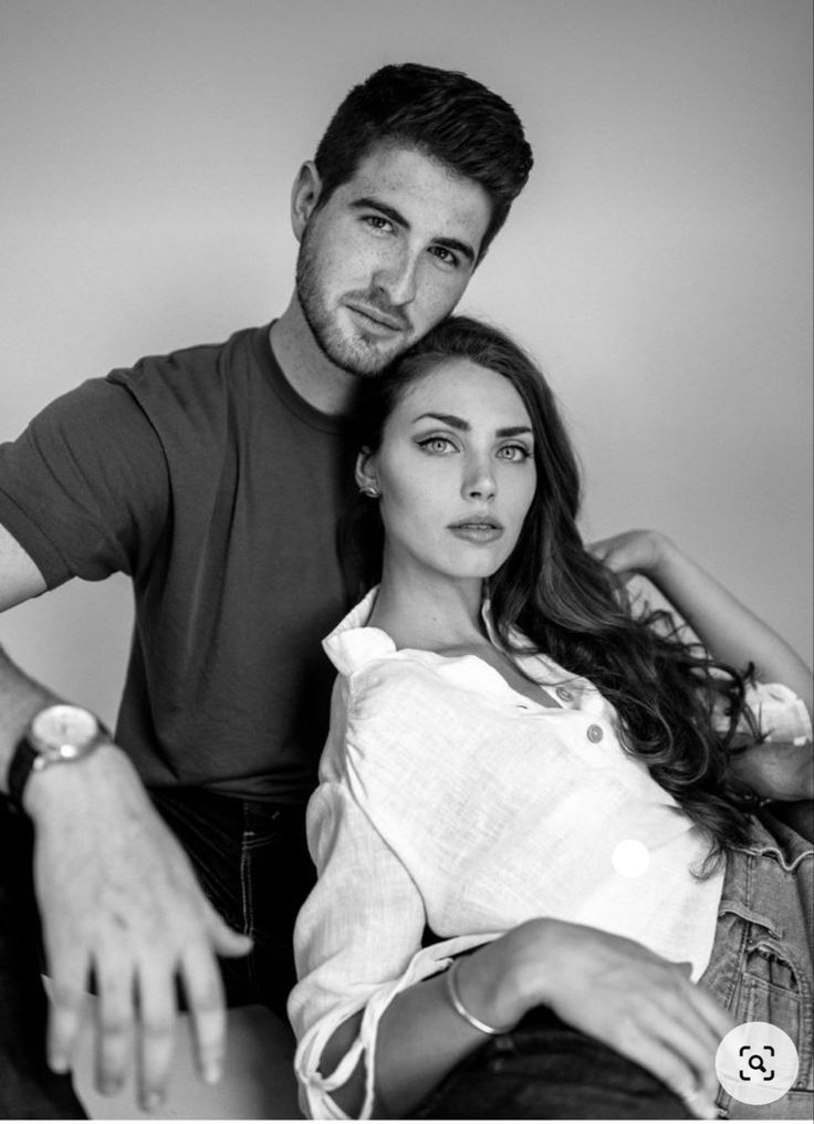 a man sitting next to a woman on top of a chair in front of a wall