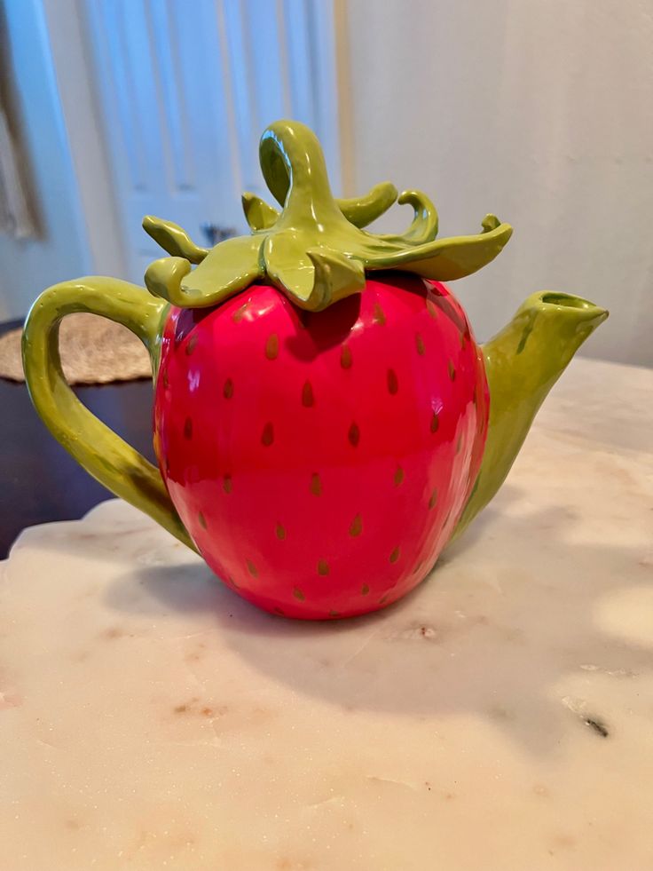 a ceramic strawberry teapot sitting on top of a table