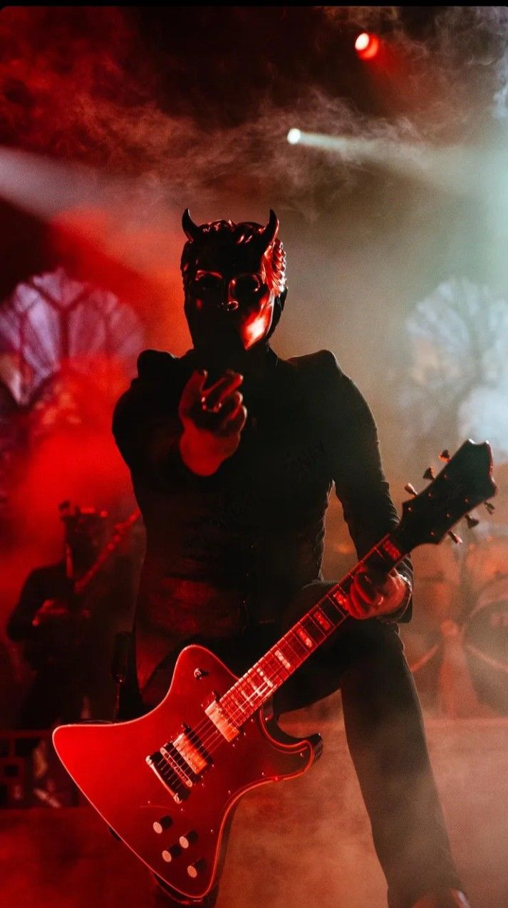 a man in a black cat mask holding a red electric guitar while standing on stage