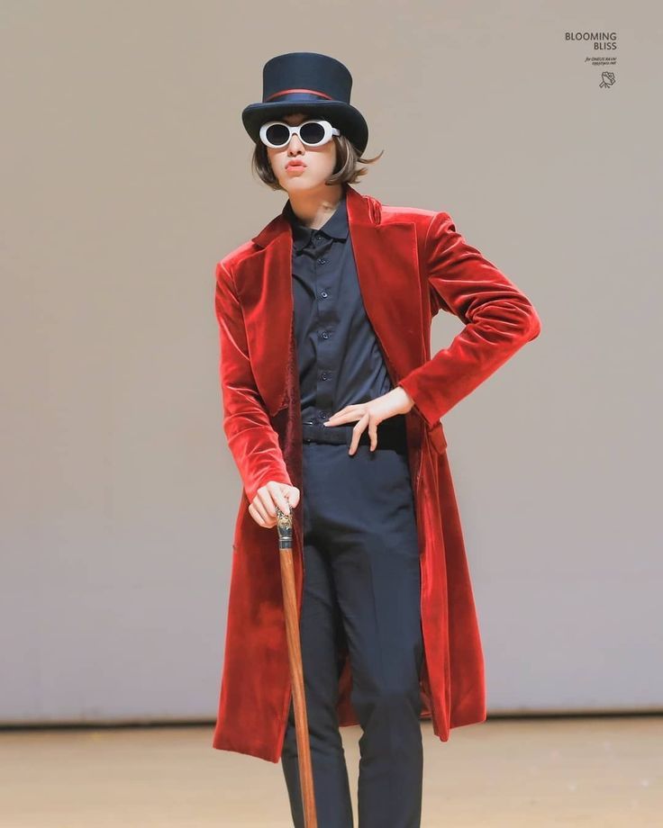 a man in a red coat and hat with a cane standing on a stage wearing sunglasses