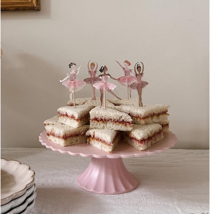 a pink plate topped with cut in half sandwiches and fairy figurines on top of it