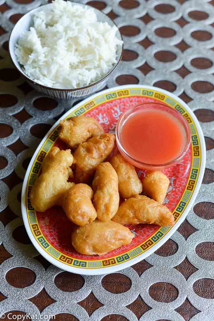 sweet and sour chicken on a plate next to a small bowl of rice with dipping sauce