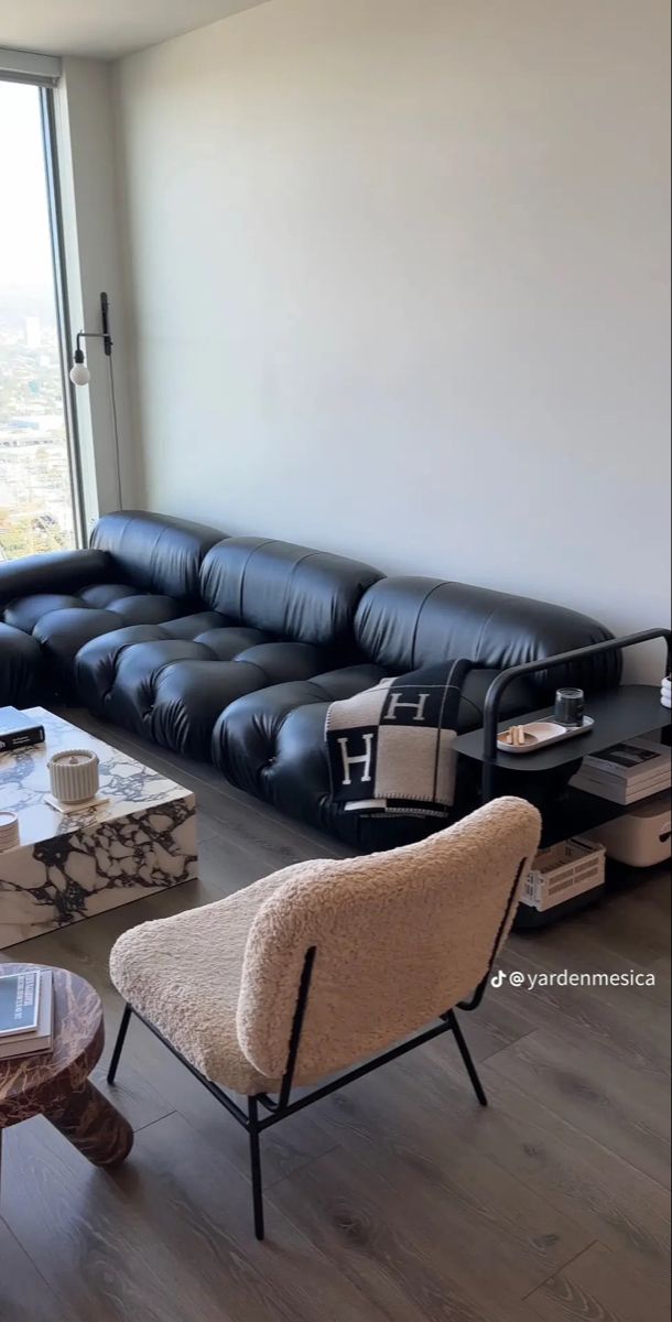 a living room with black leather couches and tables in front of a large window