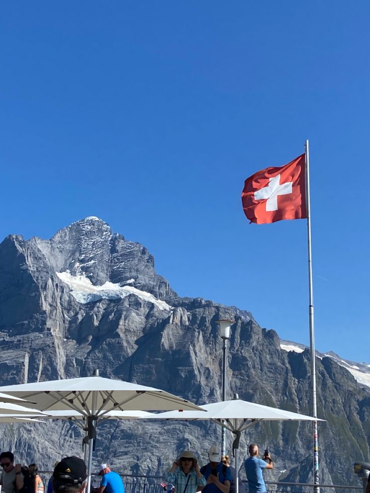 people are standing under umbrellas in front of a mountain with a swiss flag on it