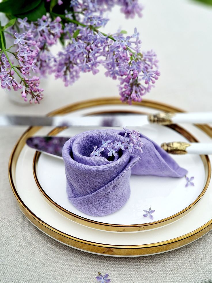 purple napkins and flowers on a white plate with gold rimmed place setting for two