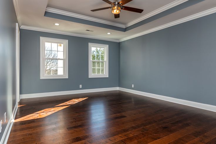 an empty room with hard wood flooring and blue walls, two windows on the far wall