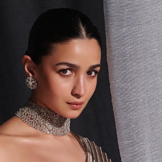 a woman in a gold dress with silver jewelry on her neck posing for the camera