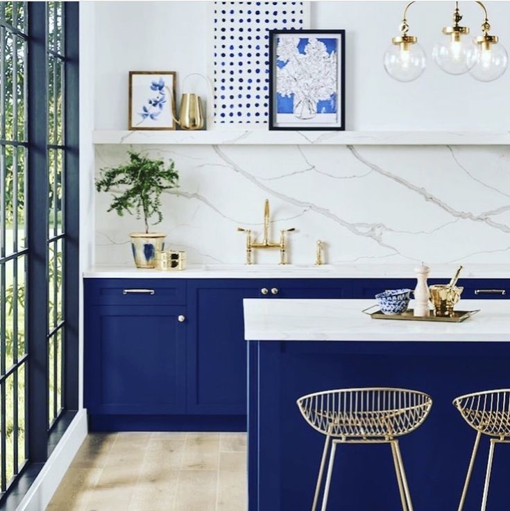 a kitchen with blue cabinets and marble counter tops, gold bar stools and brass accents