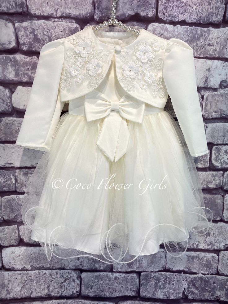 Beautiful Ivory Cream Christening and Baptism dress.    Dress and bolero set.  The 2 pieces match perfectly, the classic sleeveless dress has a satin bodice and lined skirt with layers of wired net giving the dress a full skirt look.  The pretty dress has a neat perfect 'chocolate box' bow added to the centre and ties to the rear of the dress.  The pretty matching bolero has a centre button closure, with intricate petal flower and faux pearl applique detailing either side. Available age 0 to 12 Fitted Long Sleeve Baptism Dress For Party, Elegant Fitted Off White Baptism Dress, Elegant Cream First Communion Dress For Spring, Elegant Fitted Baptism Dress For Spring, Elegant Cream Baptism Dress For Spring, Fitted Cream First Communion Dress For Spring, Cream Fitted First Communion Dress For Spring, Elegant Long Sleeve Fitted Baptism Dress, Elegant Fitted Long Sleeve Baptism Dress