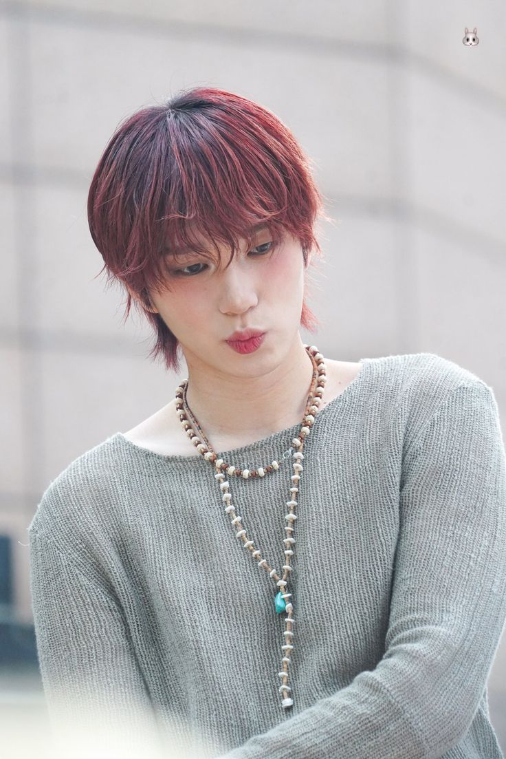 a woman with red hair is looking down at her cell phone while wearing a necklace