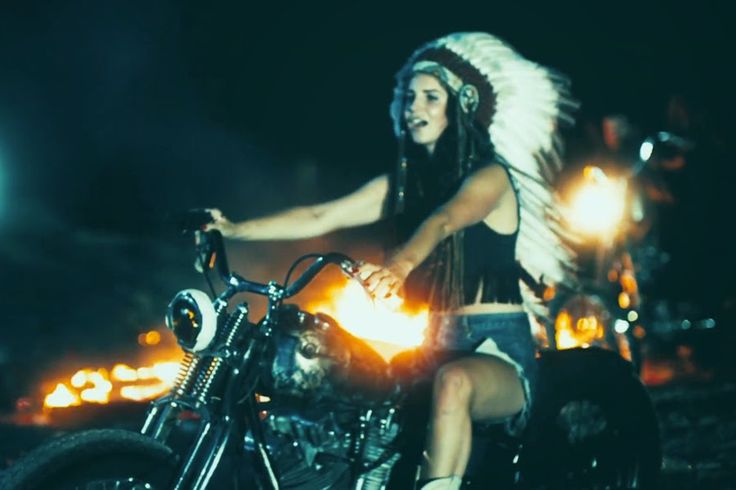 a woman riding on the back of a motorcycle in front of a fire filled street