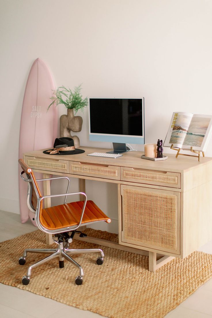 a desk with a computer, chair and surfboard