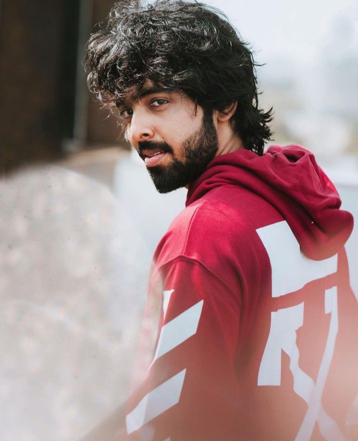 a man with curly hair and beard wearing a red hoodie looking at the camera