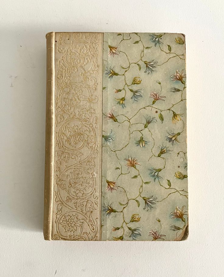 an old book sitting on top of a white wall next to a flowered cover