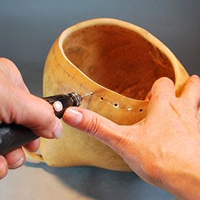 a person is using a small tool to make a vase out of wood and metal