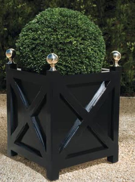 a black planter sitting on top of a stone floor next to a green bush