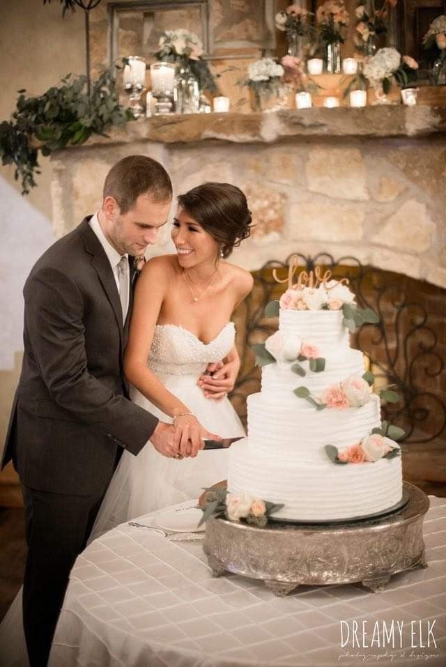 a bride and groom are cutting their wedding cake with candles on the mantle behind them