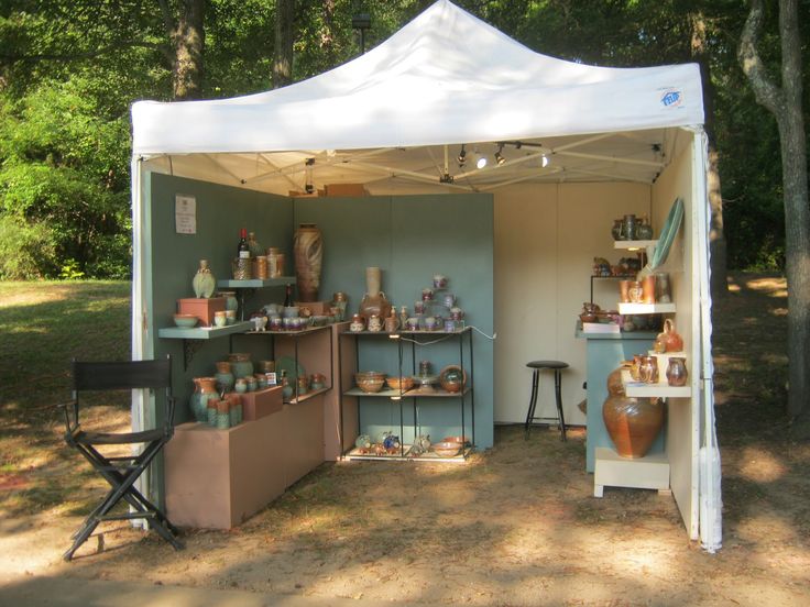 an outdoor shop with pottery on display in the shade under a canopy, surrounded by trees